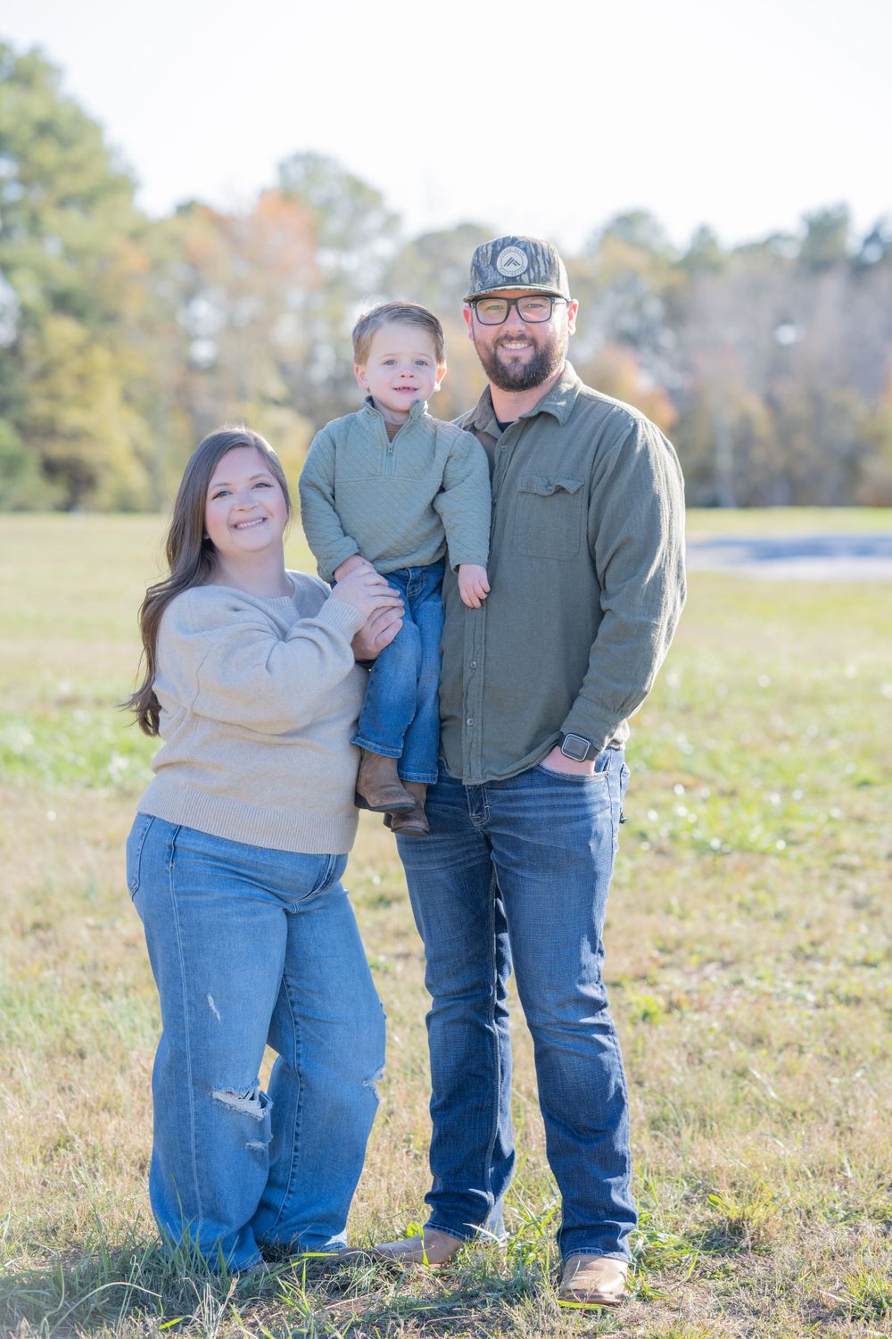 A family of three posing together outdoors on a sunny autumn day.