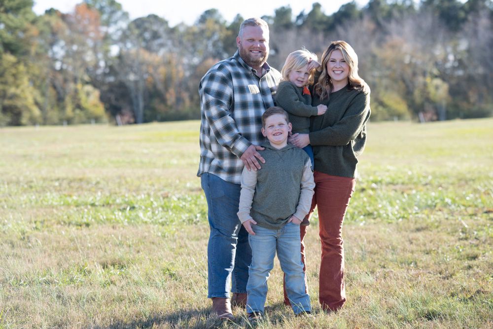 Family of four posing together in casual attire on a grassy field.