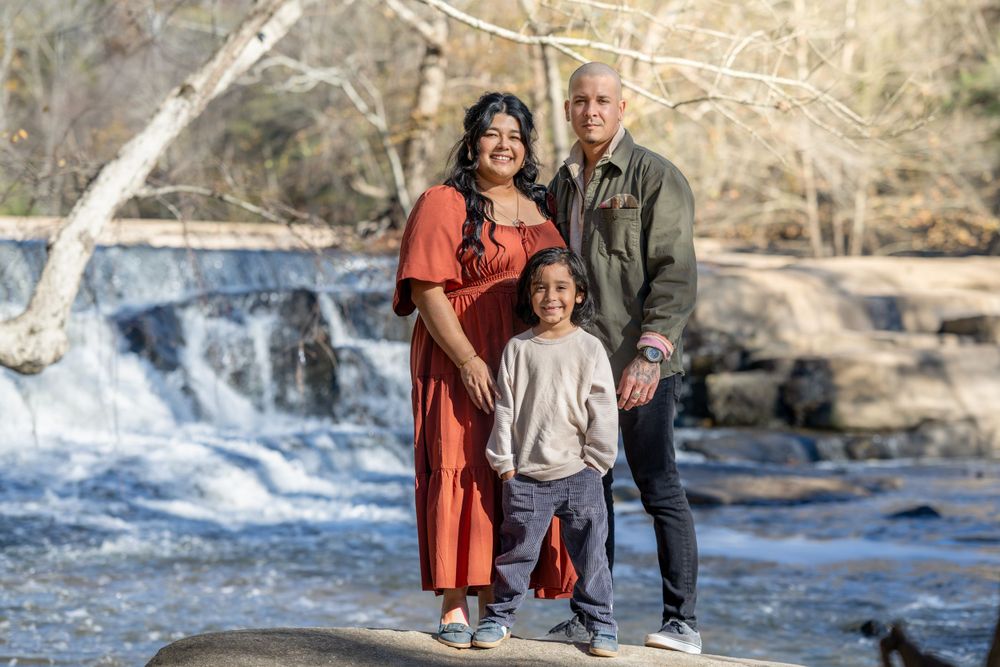 Family portrait taken in front of a scenic waterfall with rocks and trees in background.