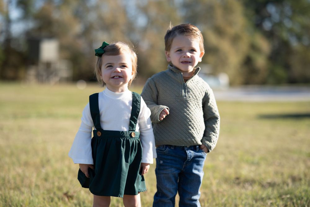 Two young children in coordinated outfits smiling outdoors on a sunny day.