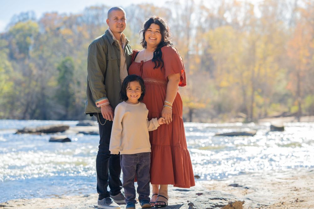 Family stands on rocks near flowing river during autumn photoshoot.