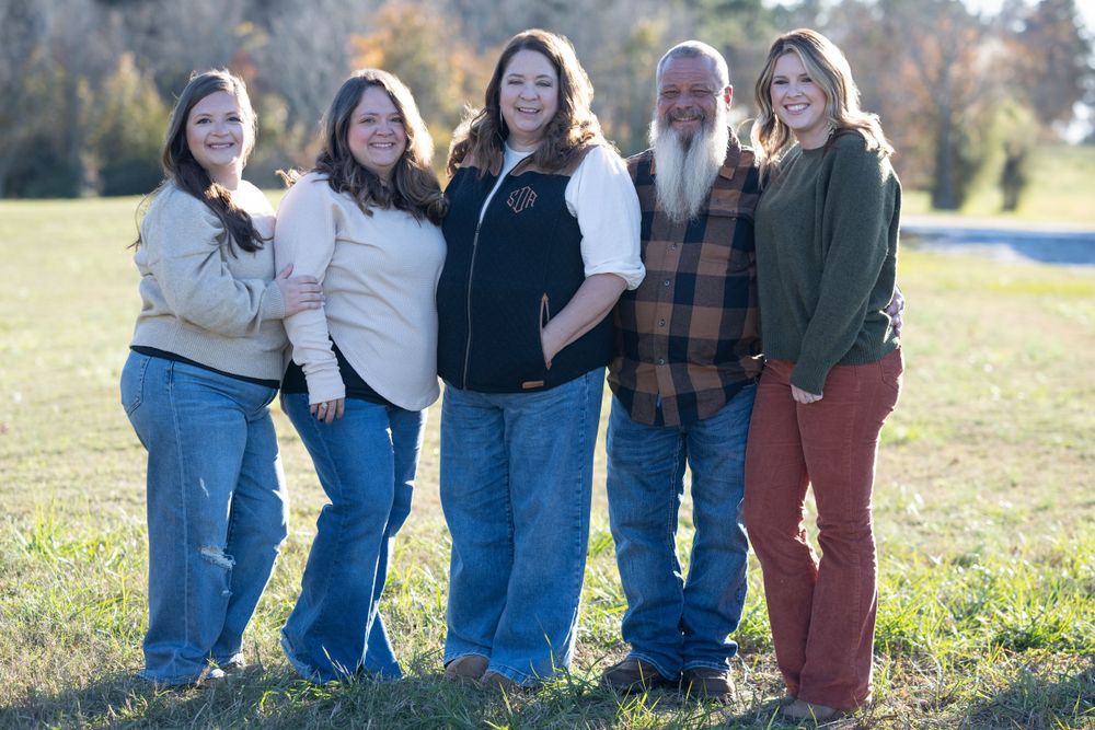 Group of five people in casual wear posing together outdoors on a sunny autumn day.
