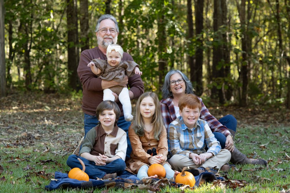 Multi-generational family group poses with pumpkins in outdoor fall setting.