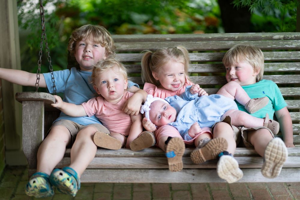 Young siblings share laughs while sitting together on wooden garden bench.