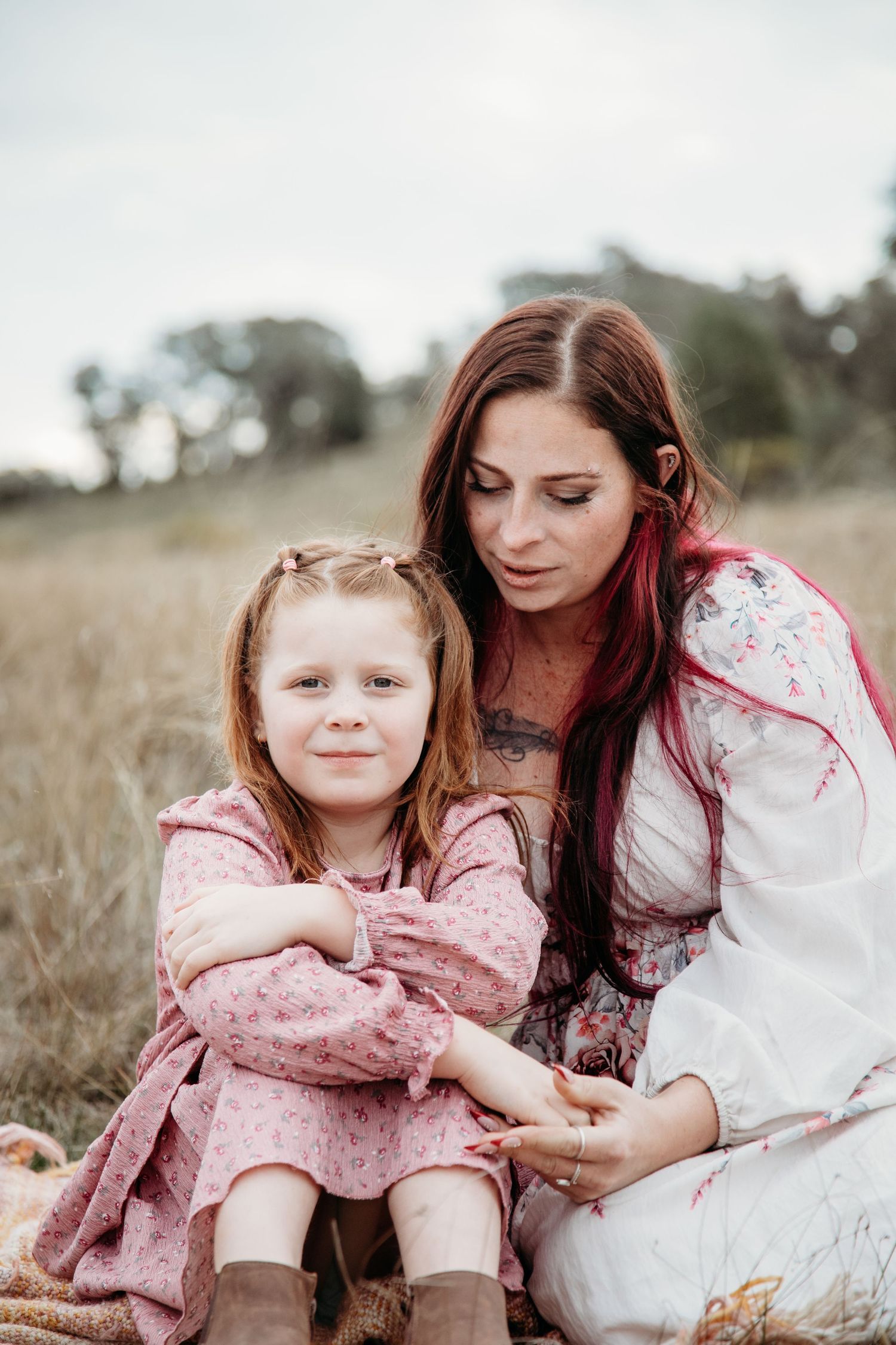 Sweet candid moments shared between parent and child sitting together in a sunlit grassy field.