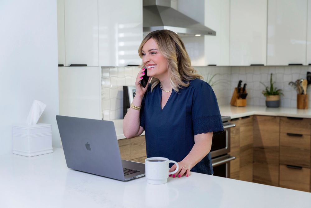Professional working remotely at home office with laptop and modern kitchen in background.