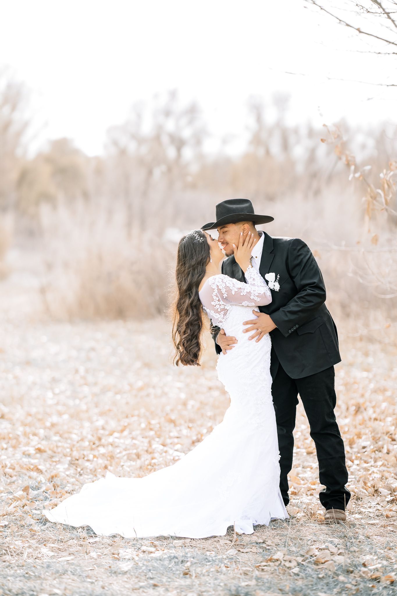 happy married couple holding hands and kissing tenderly as she wearing a white wedding dress and he wears a tuxedo posing for a picture