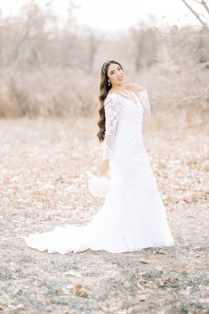 bride in a white dress posing for liz the photographer. the bride has her left hand over her chest and holdig her bouquet with her right han