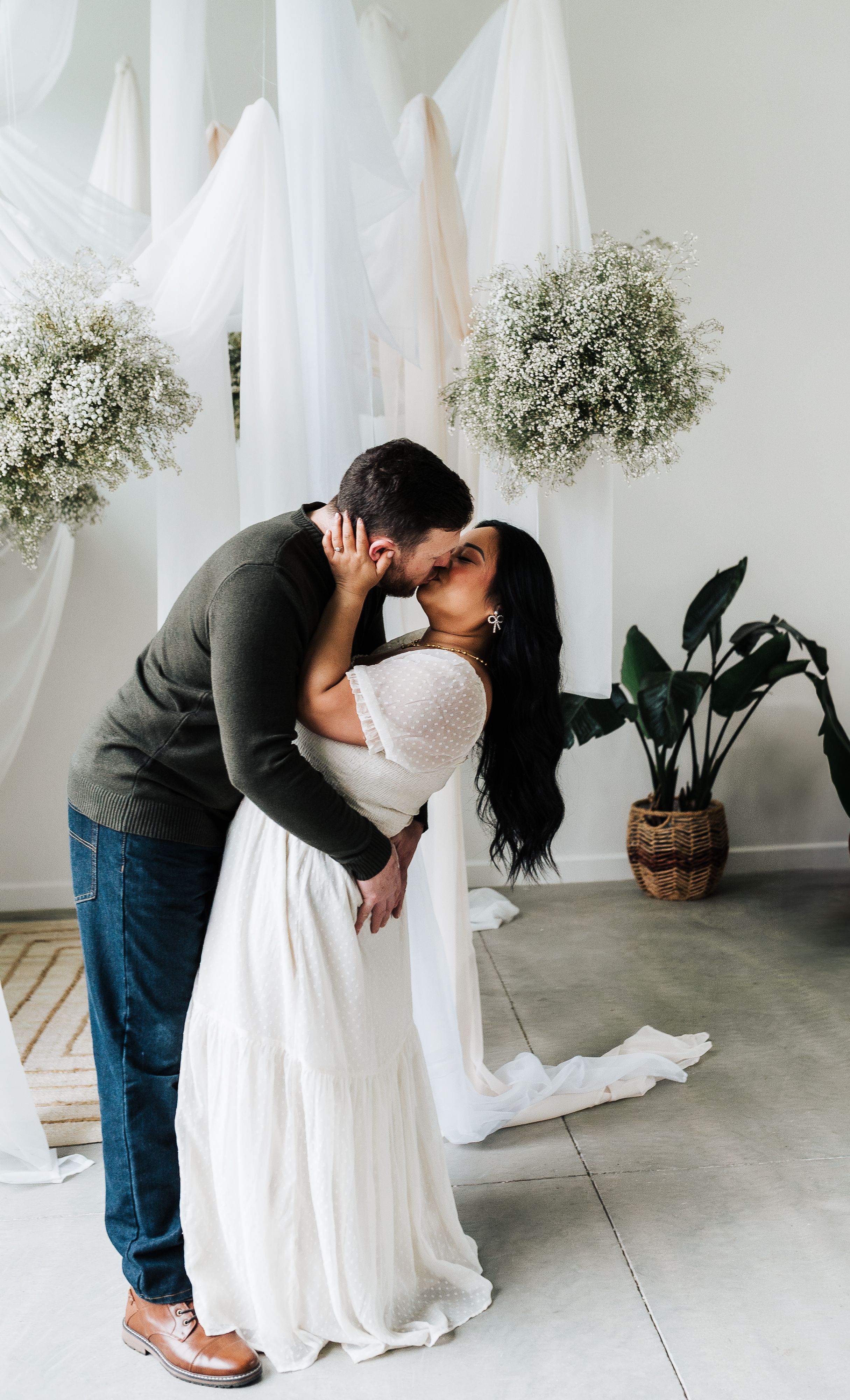 Couple sharing a romantic kiss at a boho wedding ceremony with white drapes and baby's breath floral arrangements.