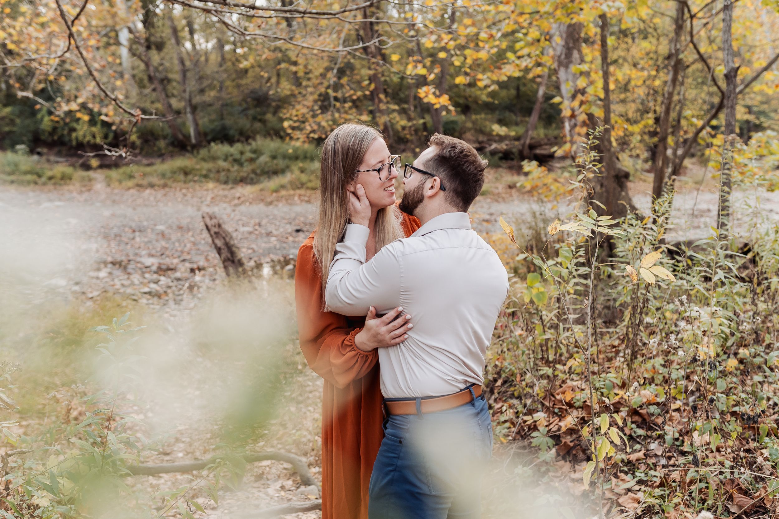 Couple sharing a romantic moment in an autumn forest setting with colorful fall foliage surrounding them.