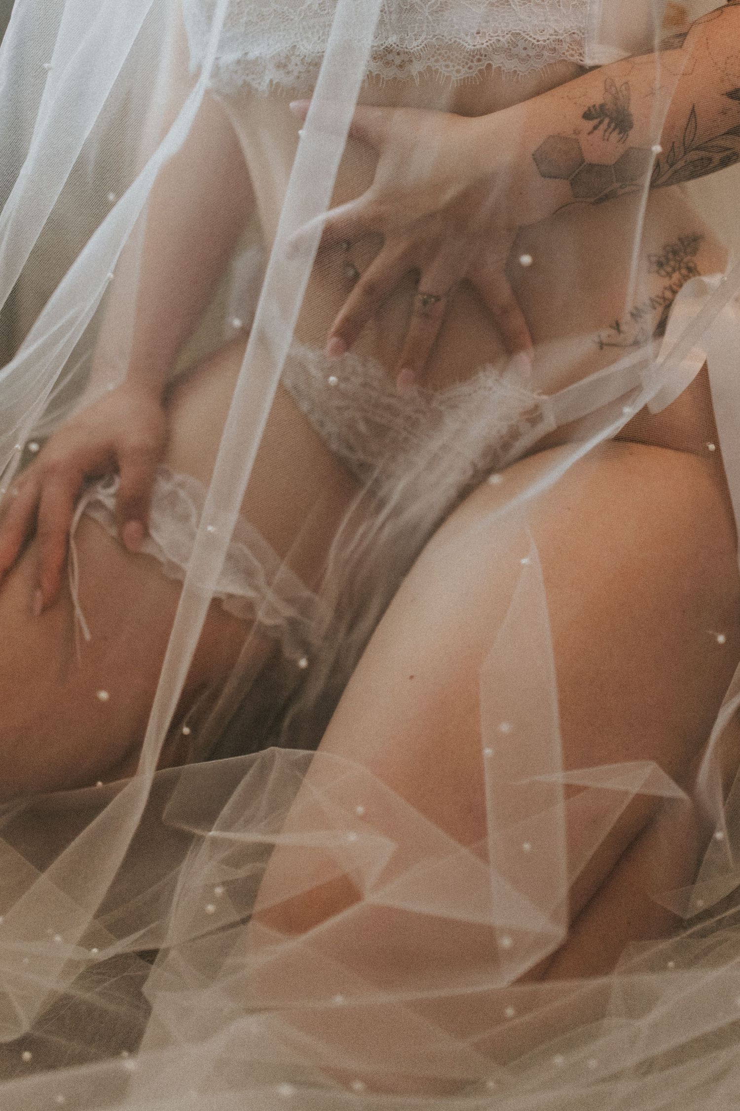 Close-up boudoir photo showing white lace lingerie and fishnet stockings against a bright window.