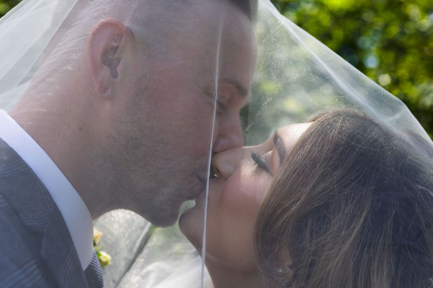 Intimate moment captured through delicate veil in sunlit garden setting.