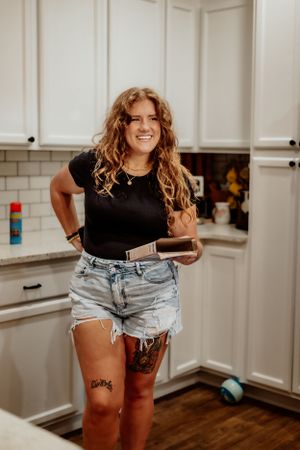 Casual indoor portrait in a modern white kitchen with person wearing denim shorts and black top.