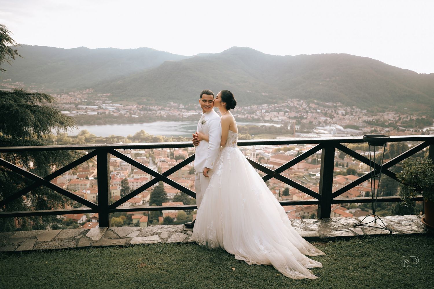 Wedding couple shares playful moment on stone terrace overlooking city view.