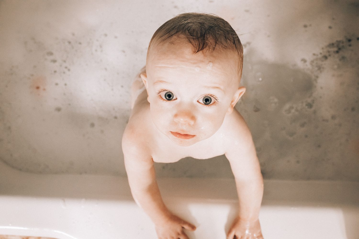 Baby taking bath and looking up with curious expression.