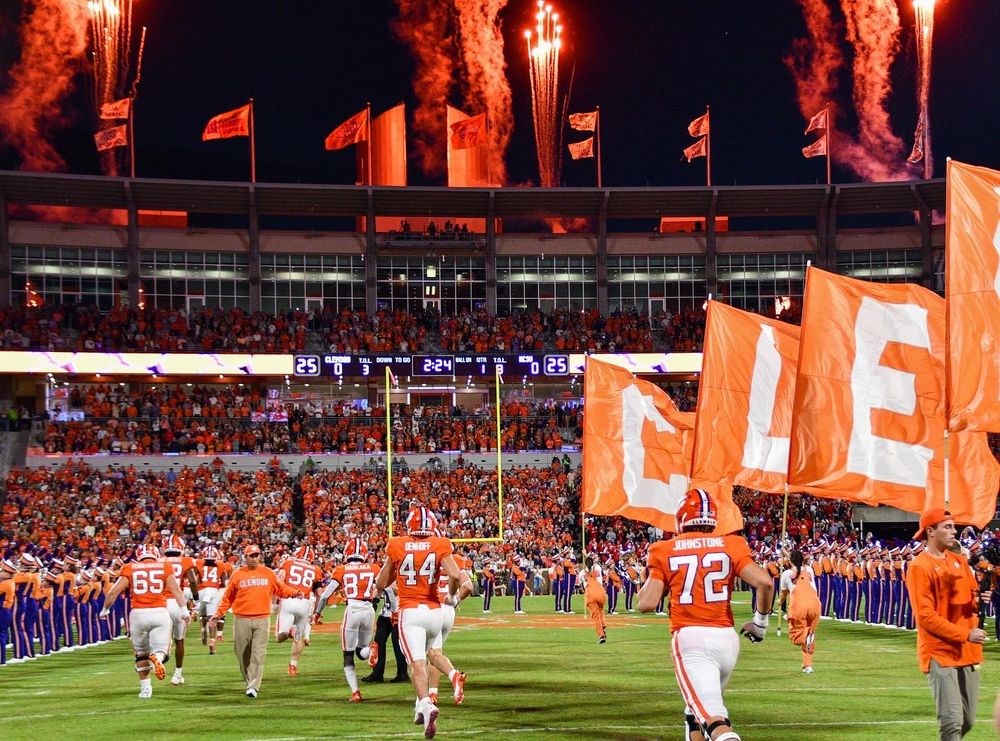 Night game celebration at Clemson Memorial Stadium with fireworks and flags illuminating the field.