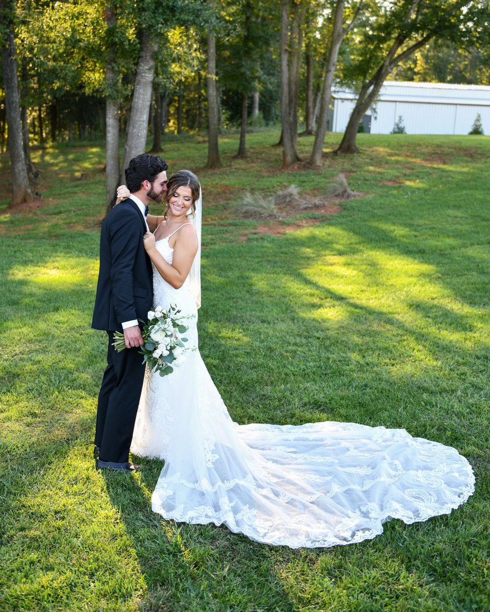 Newlywed couple embracing outdoors with bride in flowing lace train wedding dress.