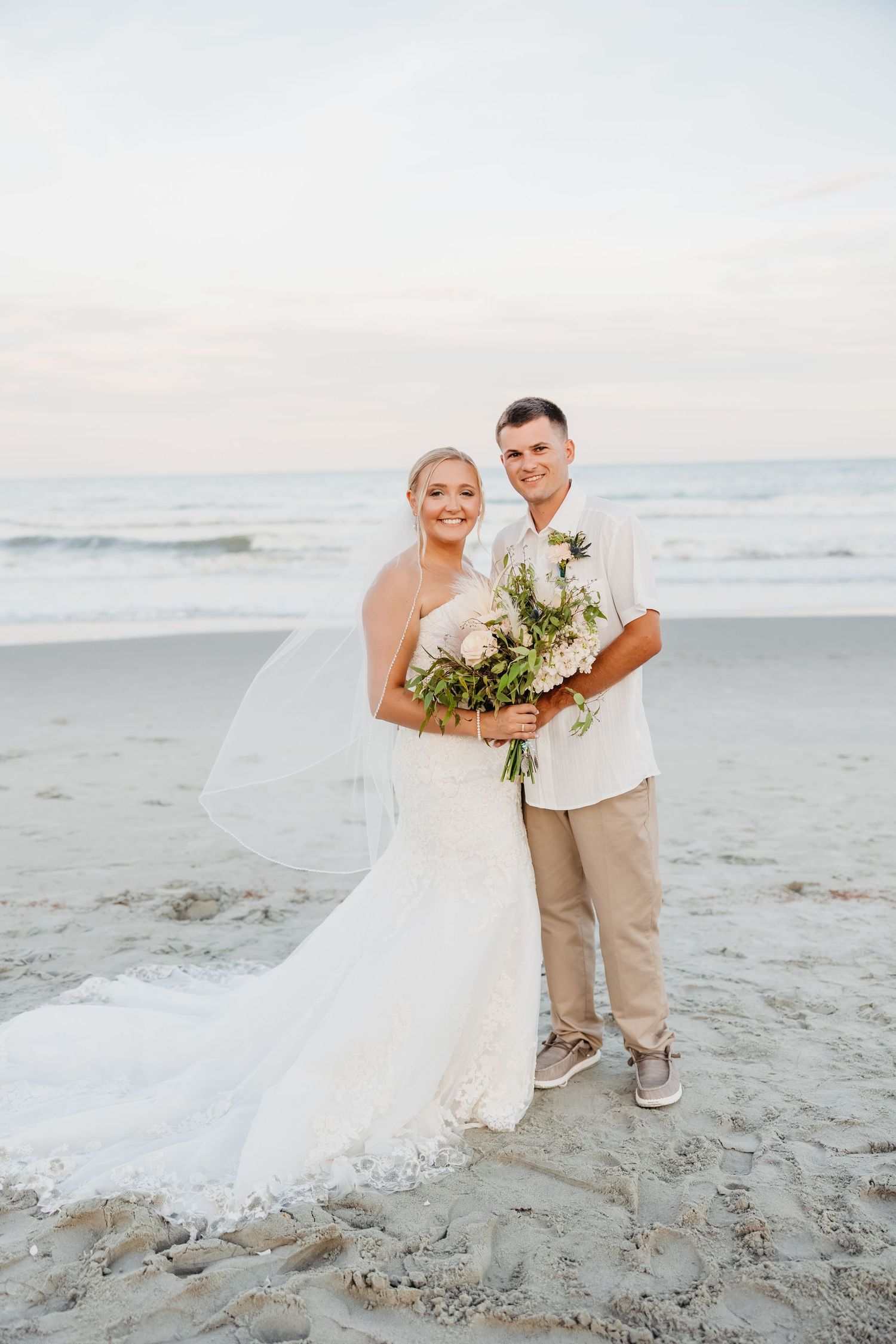 Beach wedding photos with flowing white dress and tan suit against ocean backdrop.