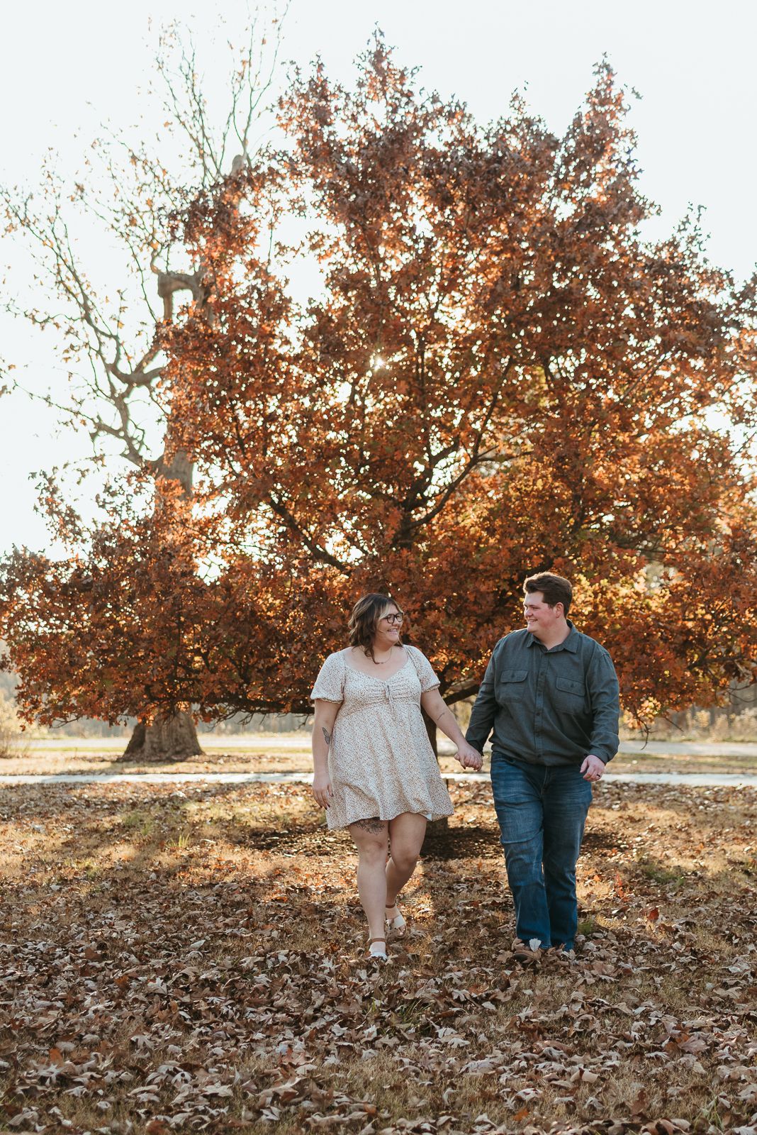Series of autumn engagement photos with couple walking through fallen leaves under golden oak trees.