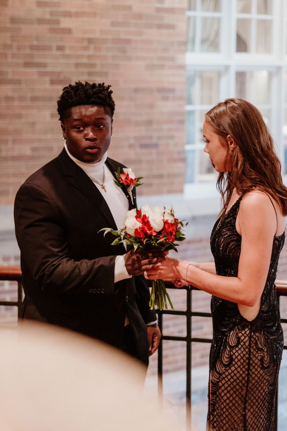 Formal event scene with two people exchanging flowers in front of a brick wall.