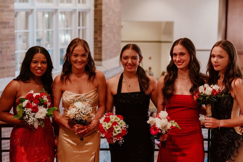 Group of bridesmaids in formal dresses holding red and white bouquets.