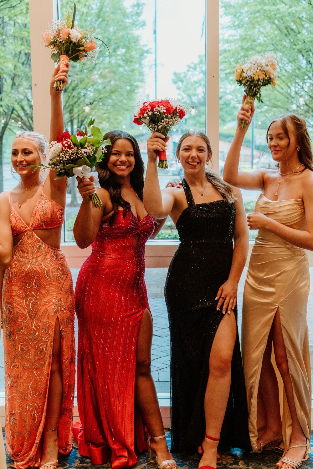 Group of friends in formal dresses holding bouquets and celebrating together.