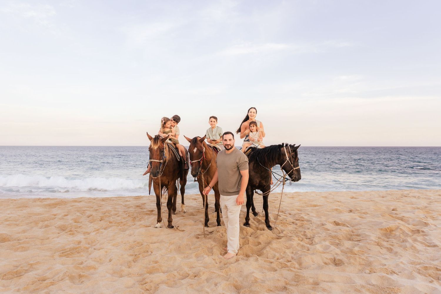 A group in coordinating blue and white outfits laughs together on a tropical beach with rocky coastline and waves.