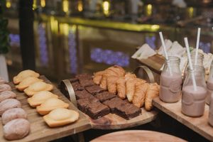 An assortment of baked goods including cookies and brownies displayed on wooden boards with milkshakes in glass bottles.