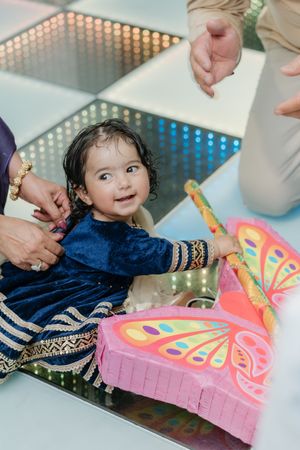Child in navy blue outfit helps cut a vibrant pink birthday cake decorated with colorful patterns.
