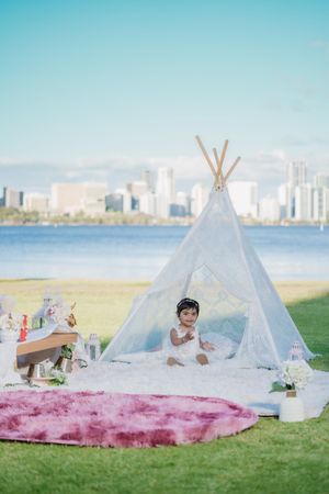 White teepee tents set up for outdoor picnic gathering on grassy area with city skyline in background.