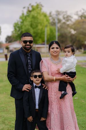 A family poses together outdoors in formal attire including a black suit and pink lace dress on a grassy lawn.