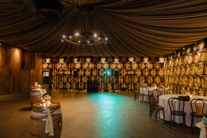 An elegant wedding reception venue with draped fabric ceiling, wine barrel decor, and turquoise accent lighting on dance floor.