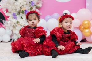 Four connected photos show a baby wearing a festive red ruffled dress sitting against a pink and white backdrop with balloons.