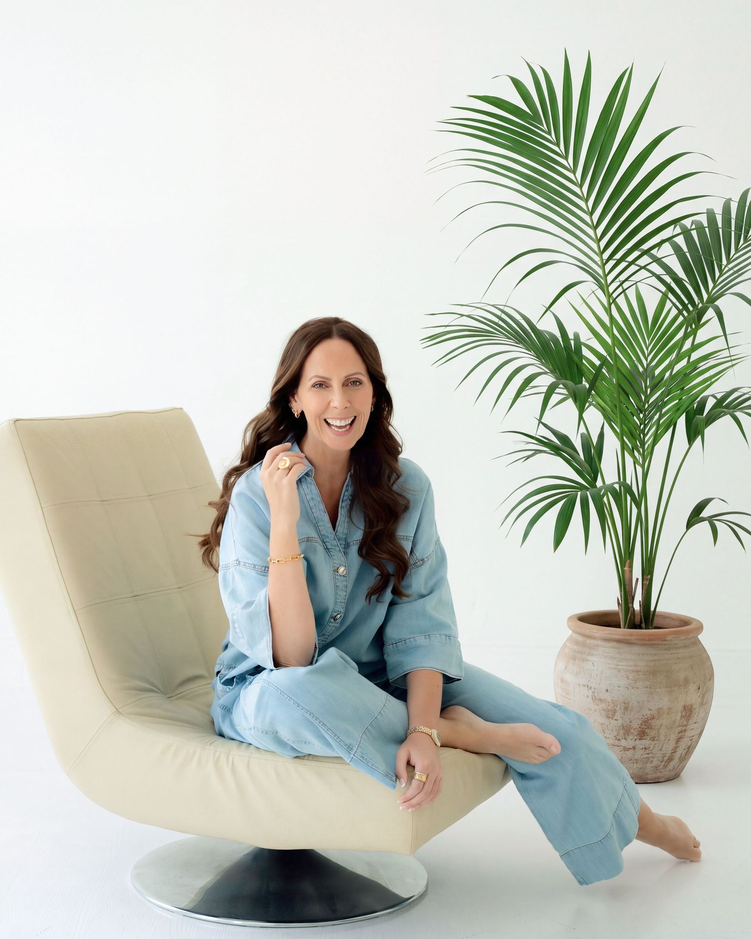 Woman in white outfit sitting on wooden chair in shallow ocean water with clear sky background.