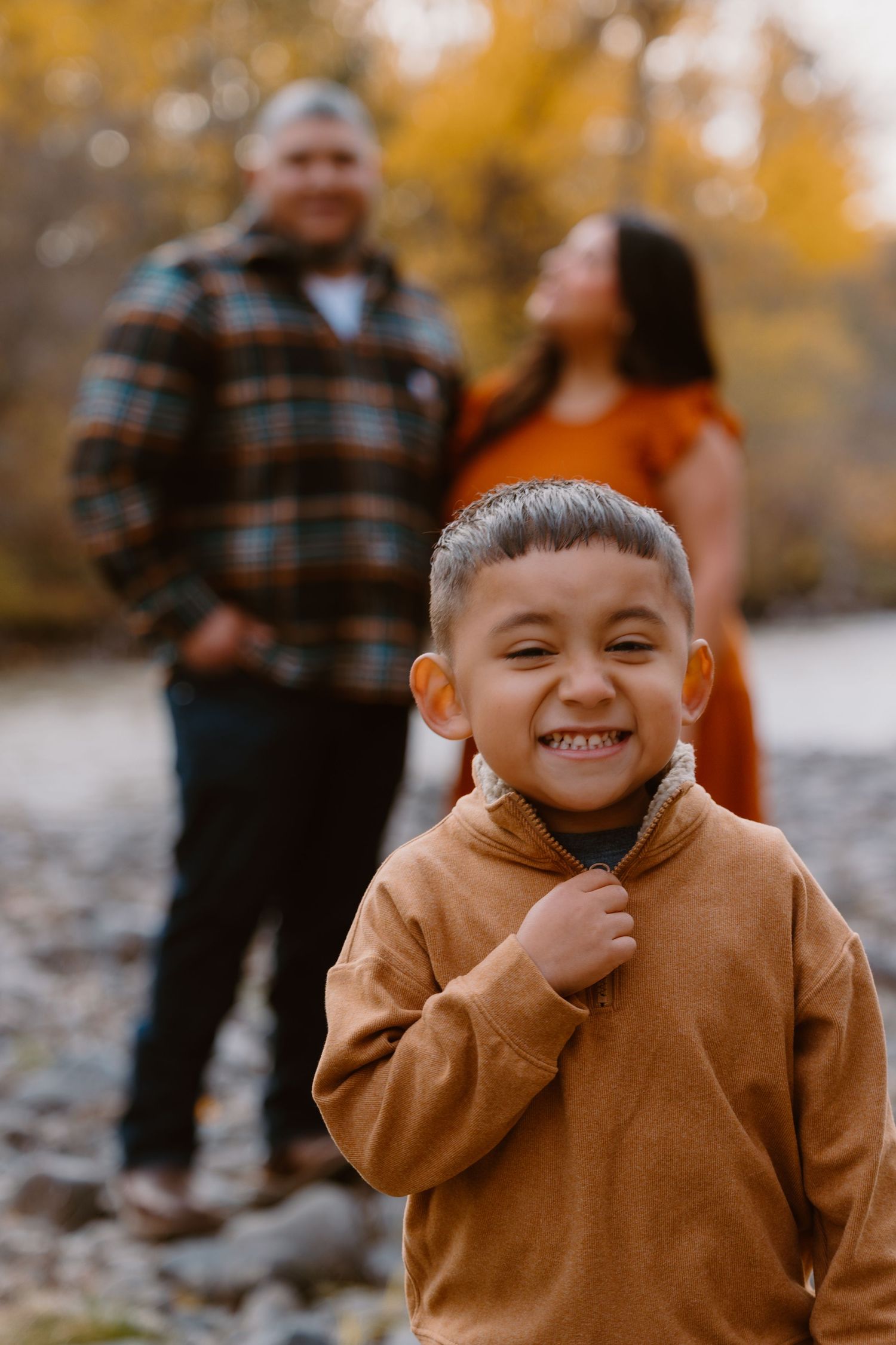 A joyful autumn family photo with a child in a brown hoodie smiling brightly.