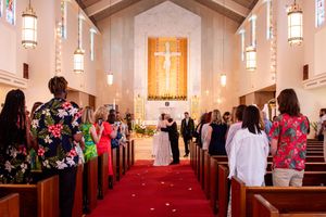 Wedding ceremony in a traditional church with white walls, hanging pendant lights, and a vibrant red carpet aisle on Oahu