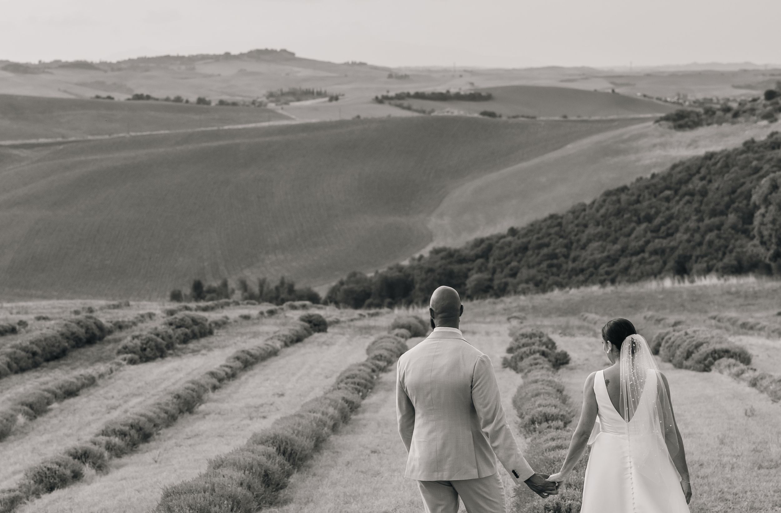 Couple walks along winding path through rolling hillside landscape on sunny day.