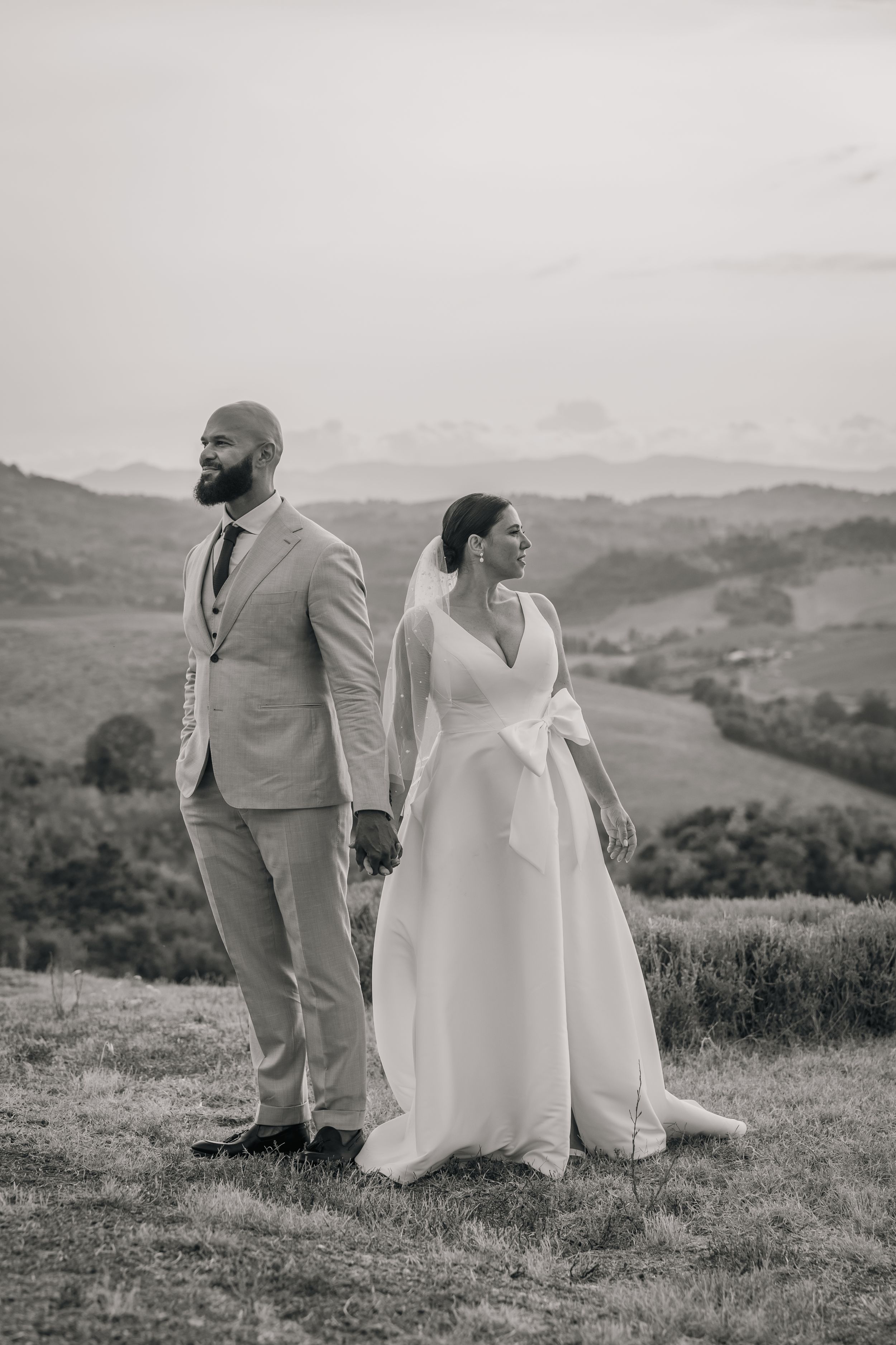 A scenic outdoor wedding photoshoot on a rolling hillside with elegant formal attire.