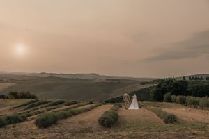A couple stands on a hilltop overlooking rolling vineyards at sunset with a misty golden atmosphere.