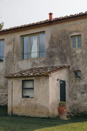 A rustic Italian villa with weathered stone walls and terracotta roof tiles against a cloudy sky.