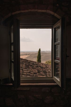 View through a rustic window frame showcasing Tuscan hills and cypress trees in the distance.