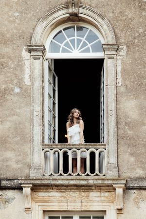 A person stands on an ornate stone balcony with arched windows and classical architectural details of a historic building.