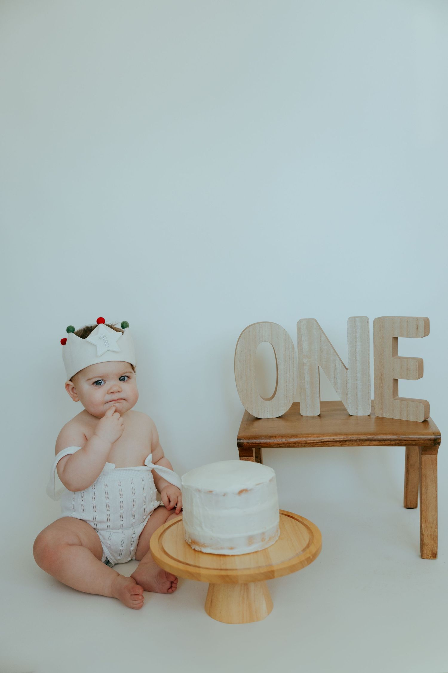 Baby in light colored outfit lying on white background with decorative ONE letters.
