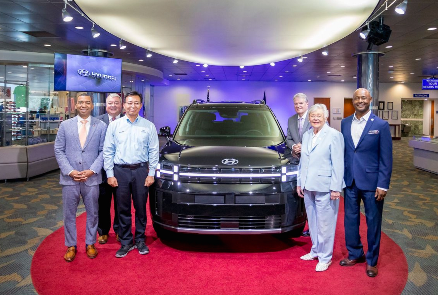 Group of people standing around new Ford vehicle on red carpet in showroom display.
