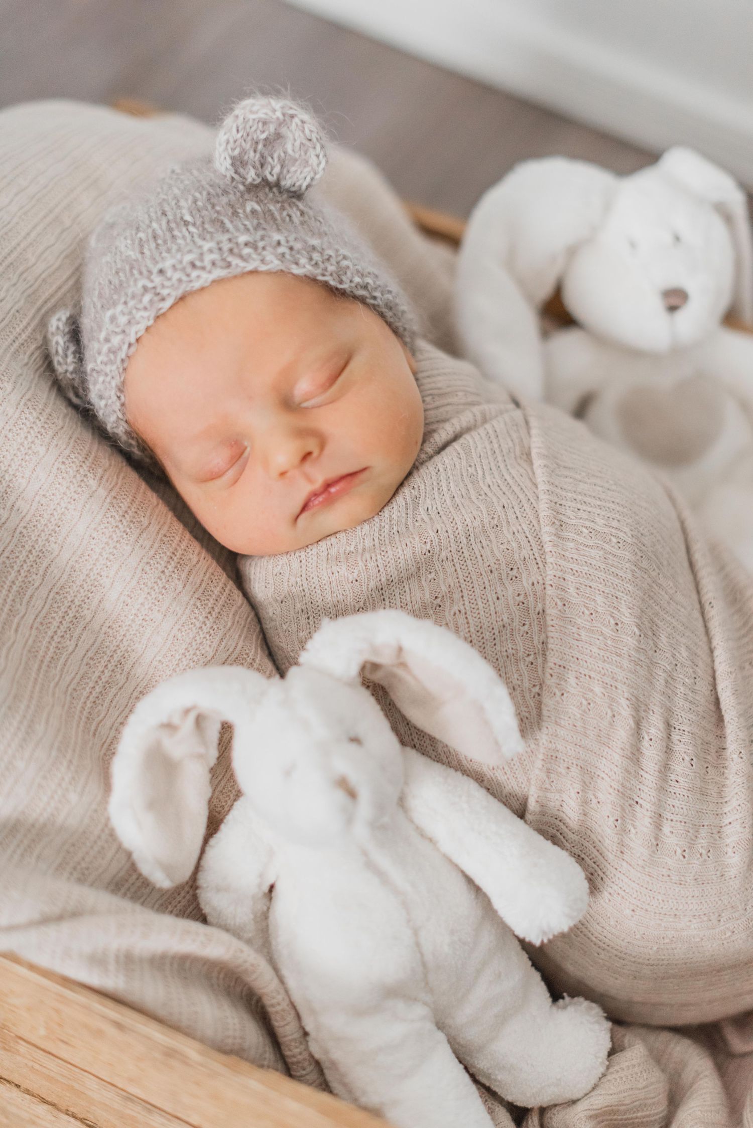 Baby in white outfit and headband lying in vintage brown suitcase with pink roses.