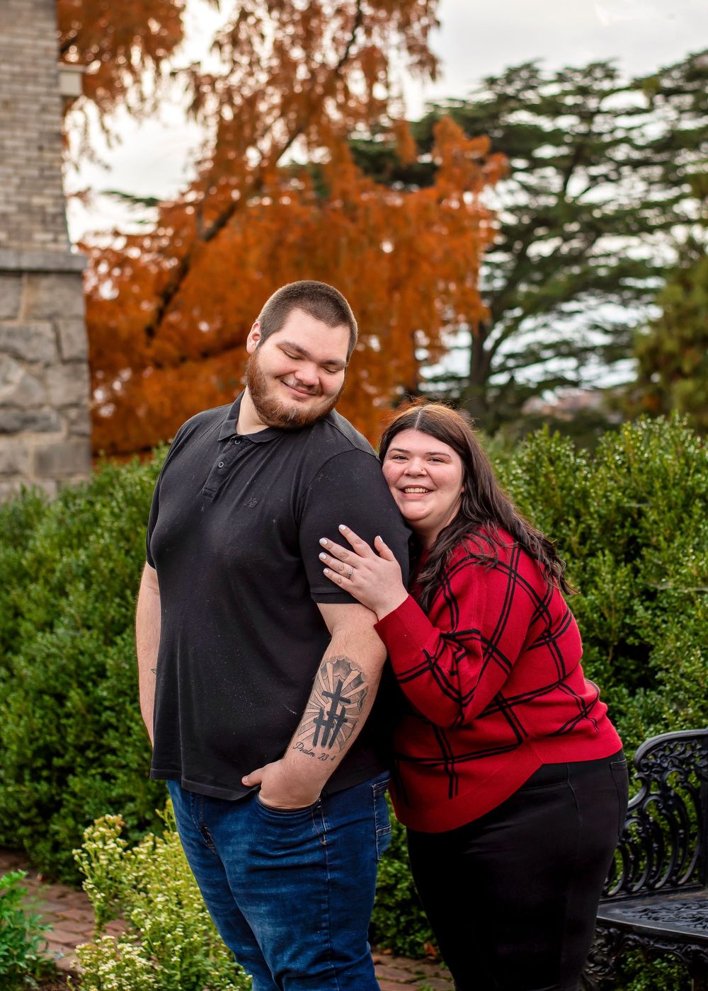 A couple shares a joyful moment together on a bench surrounded by autumn foliage and greenery.