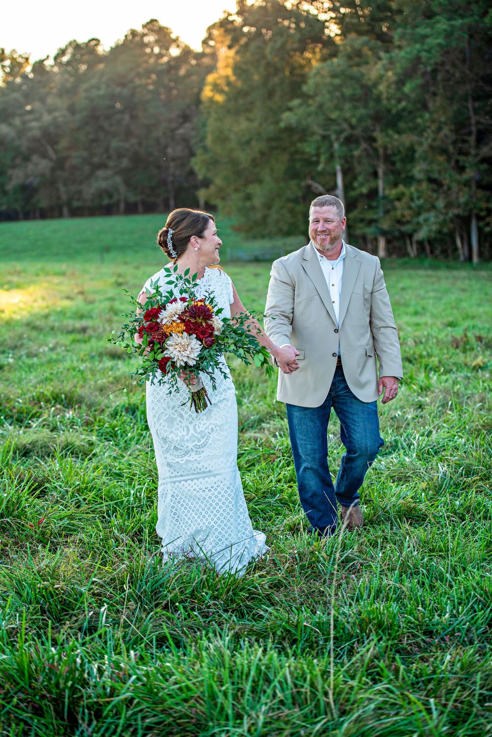 A couple walks hand in hand through a lush green field during golden hour sunset.