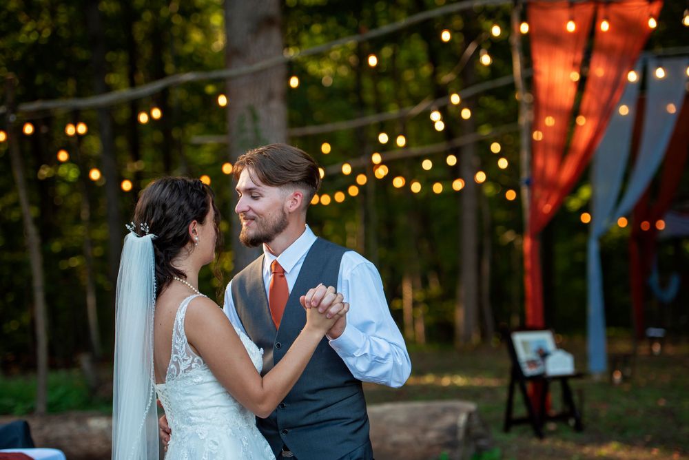 Newlyweds share their first dance under twinkling lights at an outdoor wedding reception at dusk.
