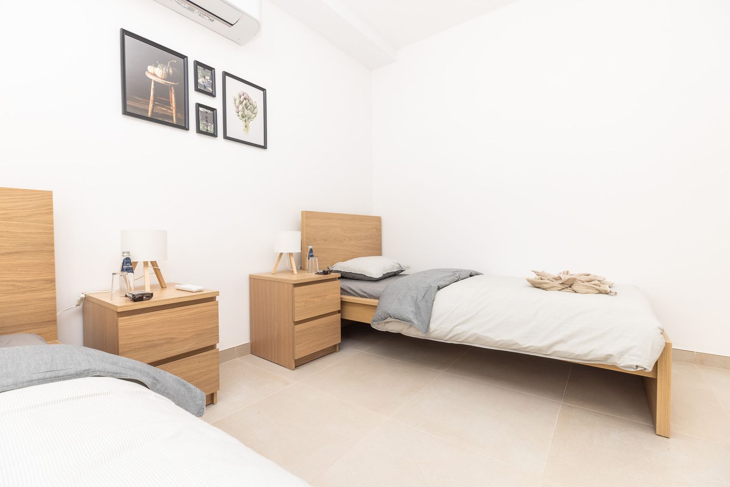Minimalist twin bedroom with matching wooden furniture, framed wall art, and bright white walls.