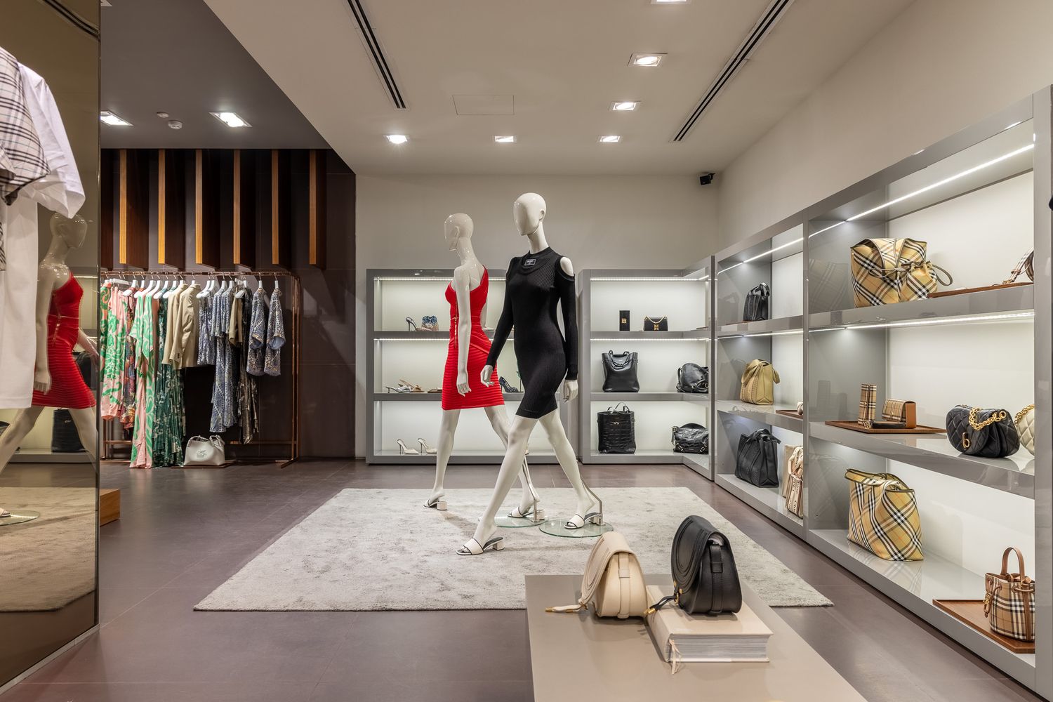 Upscale fashion boutique interior with mannequins in designer outfits, handbags, and illuminated shelving.